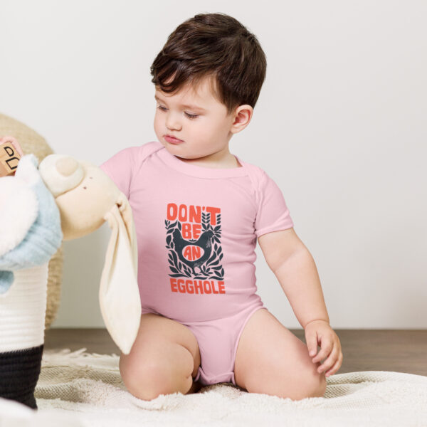 A baby in a pink onesie playing with a teddy bear.