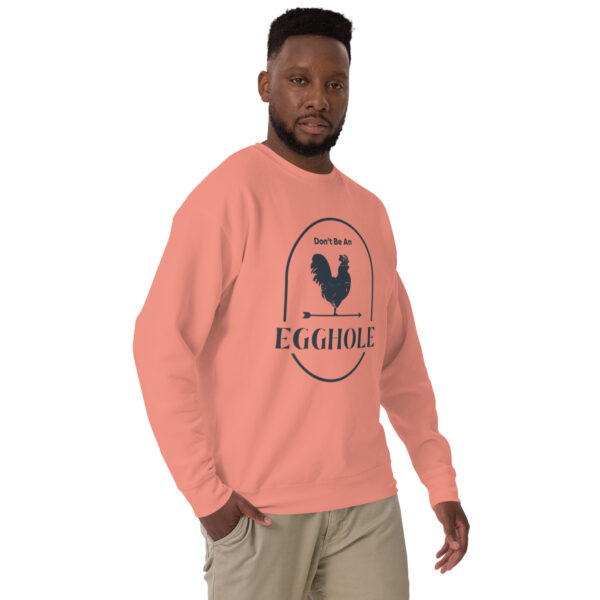 A man wearing an eggshell sweatshirt standing next to a wall.